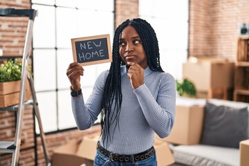 African american woman holding blackboard with new home text serious face thinking about question...