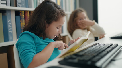 Two kids students using computer reading book at classroom