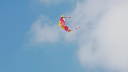 Colorful kite flying in the blue sky under gusts of wind with some white clouds up high. Hobbies and leisure activities concept. 4k Footage.
