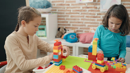 Two kids playing with construction blocks sitting on table at kindergarten