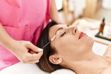 Obraz na płótnie Canvas Middle age hispanic woman having eyebrows treatment at beauty center