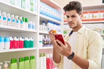 Young hispanic man customer using smartphone holding pills bottle at pharmacy