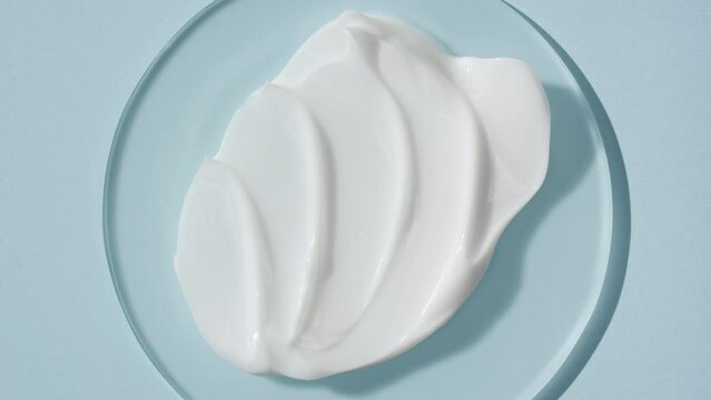 Extreme close-up top view shot of white cosmetic cream on watch glass round on pale blue background with changing lighting | Cosmetic cream advertisement