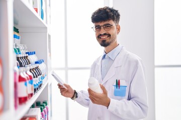 Young hispanic man pharmacist holding pills bottle reading preascription at pharmacy