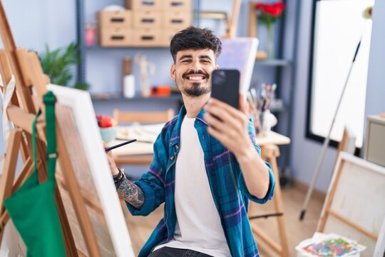 Young hispanic man artist make selfie by smartphone drawing at art studio