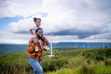 Fototapeta na wymiar Happy African American father engineer carrying his daughter playing at the Wind turbine is on vacation and escape to nature.