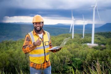 Portrait of engineer African American man working with laptop in wind turbine farm.