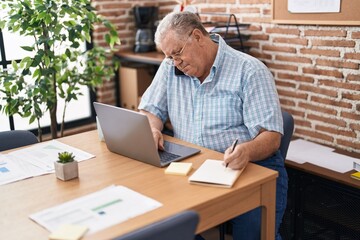 Middle age grey-haired man business worker talking on smartphone writing on notebook at office