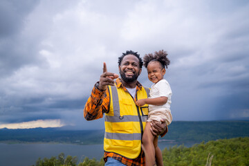 Happy African American father engineer carrying his daughter playing at the Wind turbine.