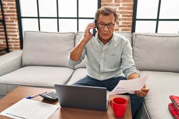 Middle age man working using laptop and talking on the smartphone at home