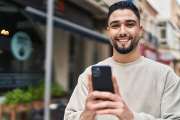 Young arab man smiling confident using smartphone at street