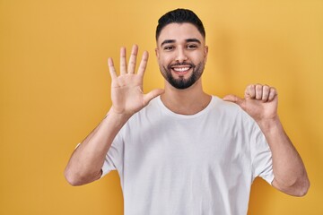 Young handsome man wearing casual t shirt over yellow background showing and pointing up with fingers number six while smiling confident and happy.