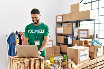 Young arab man wearing volunteer uniform using laptop at charity center