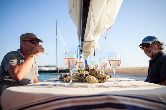 Two Men Having Oyster And Wine Tasting Onboard Sailboat, Banc D'Arguin, Arcachon Bay, France