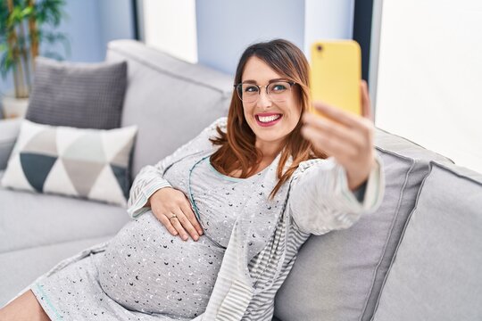 Young pregnant woman make selfie by smartphone sitting on sofa at home