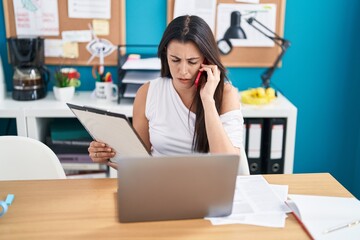 Young beautiful hispanic woman business worker talking on smartphone reading document at office