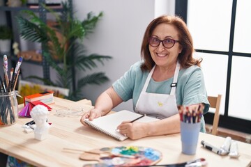 Fototapeta na wymiar Senior woman artist smiling confident drawing on notebook at art studio