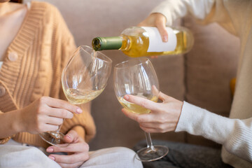 European millennial ladies in sweaters pour wine into glasses, enjoy rest, relax and free time