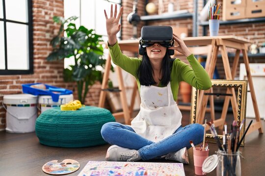 Young caucasian woman artist sitting on floor using virtual reality glasses at art studio
