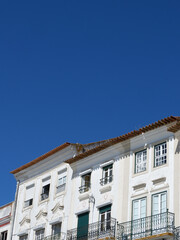 Old vintage facade of faded white colour with windows and balconies under vivid blue sky in Evora, Portugal. Vertical photo