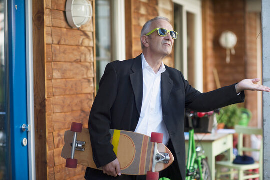 Senior businessman wearing suit and holding longboarding, Freiburg im Breisgau, Baden-W&uuml;rttemberg, Germany