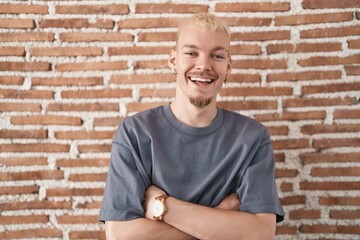 Young caucasian man standing over bricks wall happy face smiling with crossed arms looking at the camera. positive person.