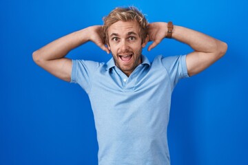 Naklejka premium Caucasian man standing over blue background crazy and scared with hands on head, afraid and surprised of shock with open mouth