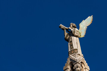 Cherub Angel blowing trumpet. A medieval 13th century statue a the top of St Michael Church in Lucca (with blue sky and copy space)