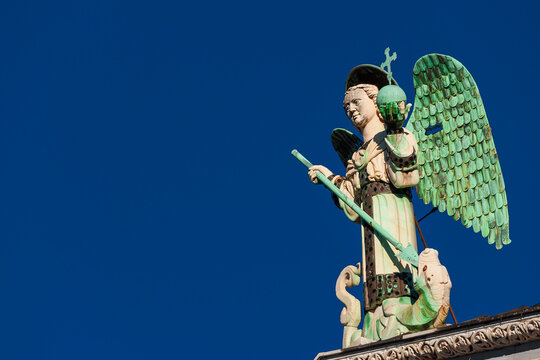 Saint Michael the Archangel defeats the Dragon, a medieval 13th century statue a the top of St Michael Church in Lucca (with blue sky and copy space)