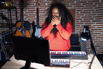 Plus size hispanic woman playing piano at music studio shocked covering mouth with hands for mistake. secret concept.