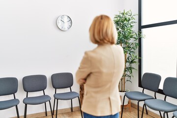 Middle age blonde woman on back view looking clock at waiting room
