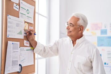 Middle age grey-haired man business worker writing on cork board at office