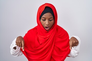 Young arab woman wearing traditional islamic hijab scarf pointing down with fingers showing advertisement, surprised face and open mouth
