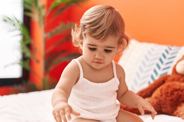 Adorable hispanic toddler sitting on bed with relaxed expression at bedroom