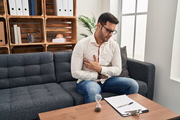 Fototapeta premium Young hispanic man with beard working at consultation office with hand on stomach because indigestion, painful illness feeling unwell. ache concept.