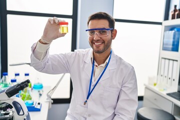 Young hispanic man scientist looking urine test tube at laboratory