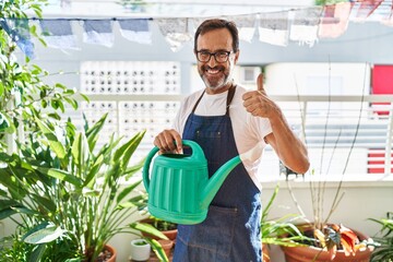 Middle age man wearing gardener apron holding watering can at home terrace smiling happy and positive, thumb up doing excellent and approval sign © Krakenimages.com
