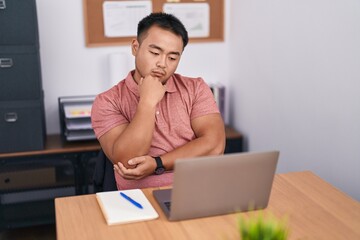 Young chinese man business worker using laptop with doubt expression at office