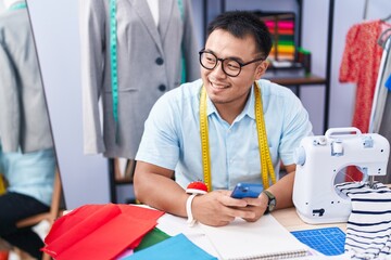 Young chinese man tailor smiling confident using smartphone at tailor shop