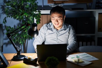 Young chinese man working using computer laptop at night winking looking at the camera with sexy...