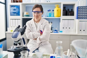 Fototapeta premium Hispanic girl with down syndrome working at scientist laboratory skeptic and nervous, disapproving expression on face with crossed arms. negative person.