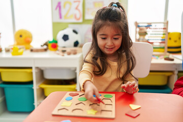 Adorable hispanic girl playing with maths puzzle game sitting on table at kindergarten