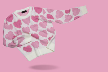 White knitted sweater, as if floating, with a pattern of pink hearts and pearls, on a pink background