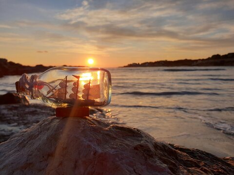Sunrays pass through a glass bottle with ship insid. Beautiful sea sunset background. Dream of travel. Souvenir from the sea.