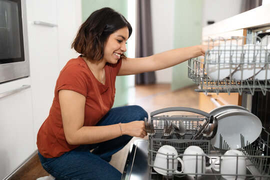 Portrait Of Young Arab Female Unloading Dishwasher Machine In Kitchen
