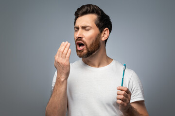 Bad breath. Handsome middle aged man checking his breath with his hand, blowing to it, standing...