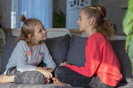 A teenage girl and her sister look at each other and talk while sitting at home. The concept of trusting relationships and help in solving the problem, understanding and friendship