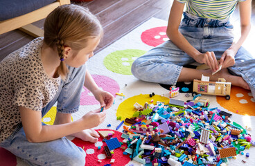  Two little sister girls play with colorful toy blocks at home in the living room. Build a  house out of bricks. The development of fine motor skills of the hands