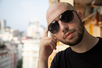 Young Caucasian confident man in sunglasses looking at camera thoughtfully. Masculine bald guy...