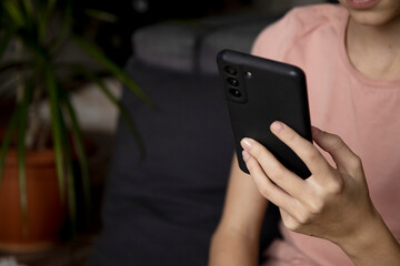 A close-up image of a teenage girl's hands using a smartphone at home in the living room, the concept of social networking, a set of SMS messages to her friends and classmates.